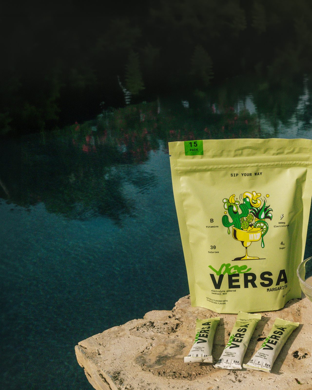 Vice Versa Margarita 15-pack pouch, three stick packs and a poured margarita on a stone ledge above a dark pool